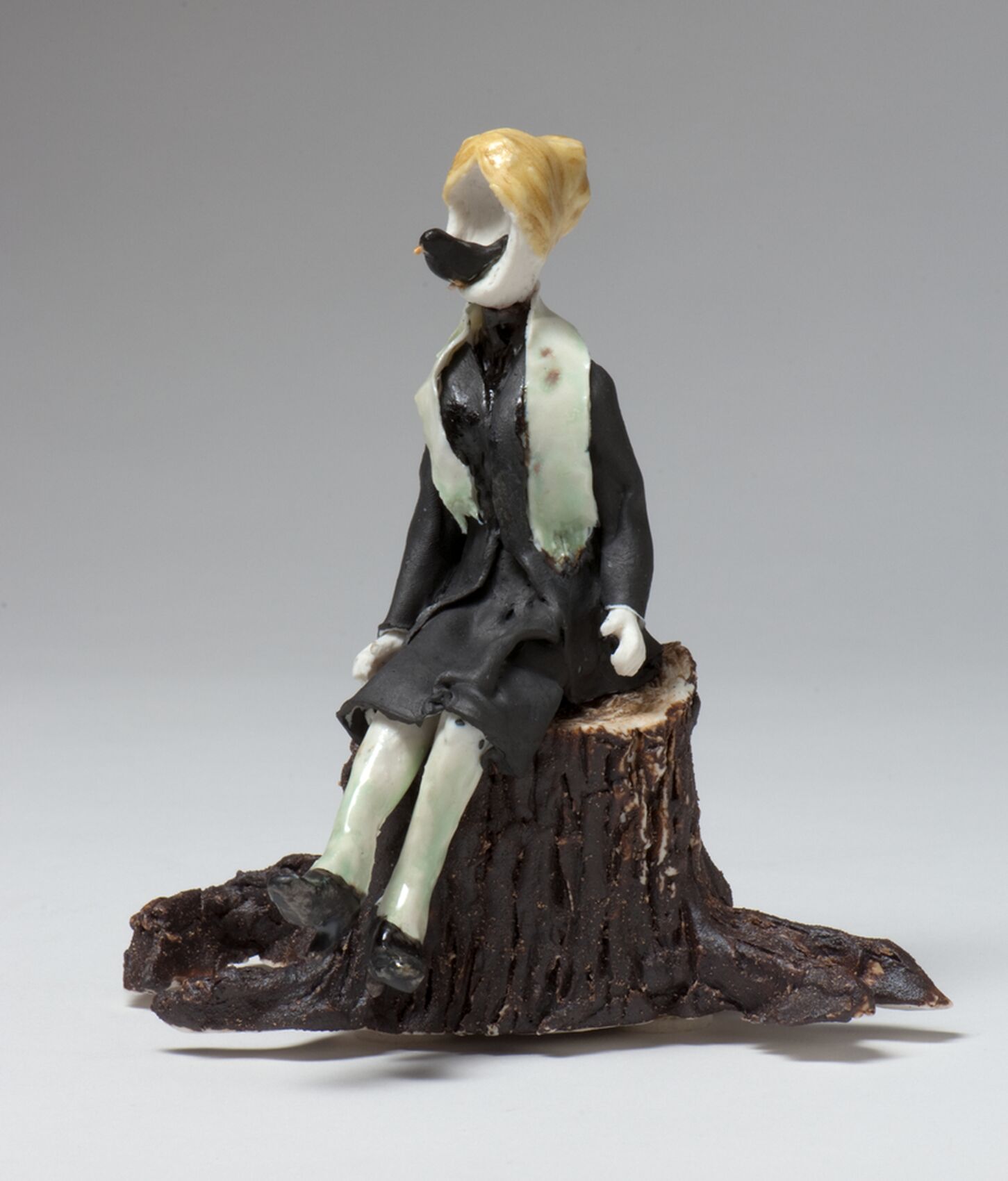 Figurine portraying a child sitting on a stump. The head has a hole where a crow is sitting.