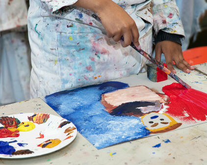 Händerna på ett barn som målar ett porträtt med akrylfärg.