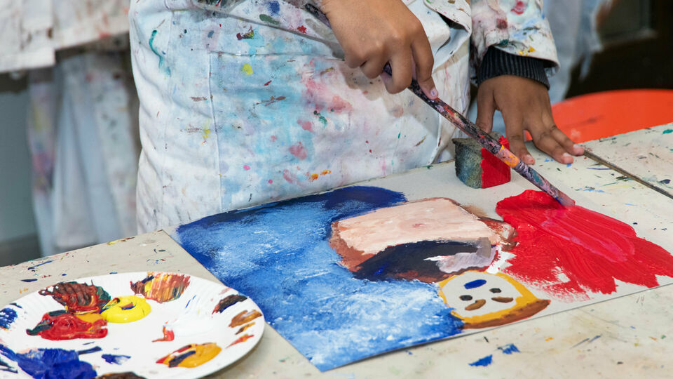 Händerna på ett barn som målar ett porträtt med akrylfärg.