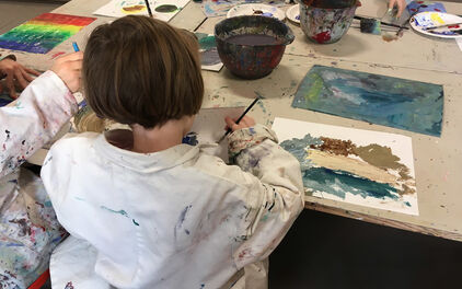 Barn som sitter vid bord i en ateljé och målar med vattenfärg.