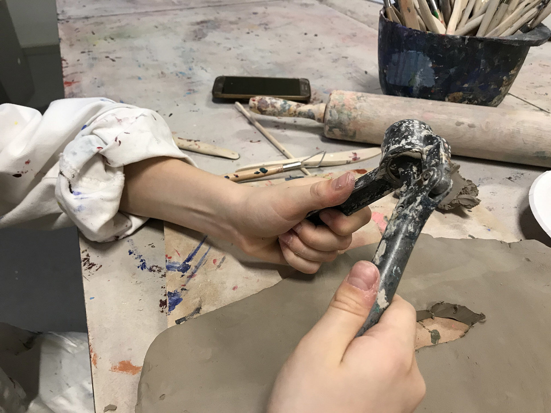 Ett par barnhänder som använder sig av en vitlökspress för att forma lera. Lera och verktyg i bakgrunden.