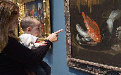 En kvinna håller en baby i famnen och tillsammans tittar de på en tavla med en röd fisk.