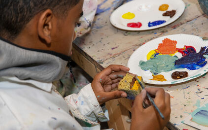 Ett barn som sitter vid ett bord i en ateljé och duttar akrylfärg på en svamp.