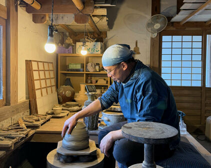 En man som sitter på huk och drejar i en keramikverkstad.