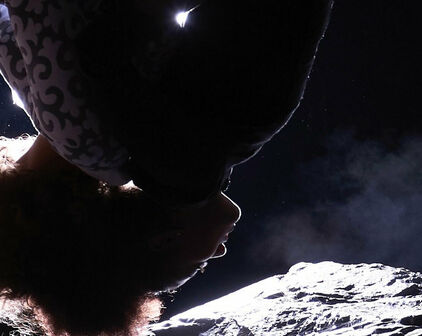 En person som tycks hänga upp och ner, med månlandskap bakom sig.