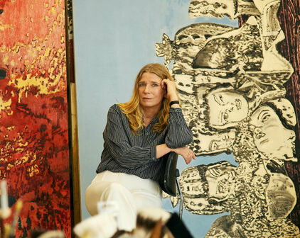 Fotografiskt porträtt av en kvinna - konstnären Karin Mamma Andersson - som sitter bland målningar i en ateljé